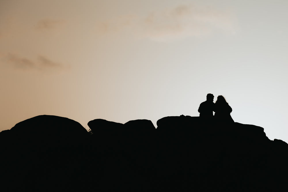 silhouetted people sitting on rocks by the setting sun