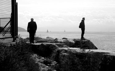 silhouetted people standing by body of water in monochrome