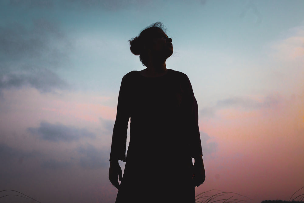 silhouetted person looks up as the sunsets behind them