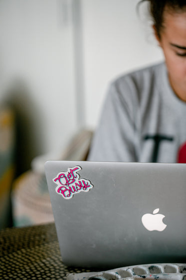 silver laptop with a pink sticker thats says get busy