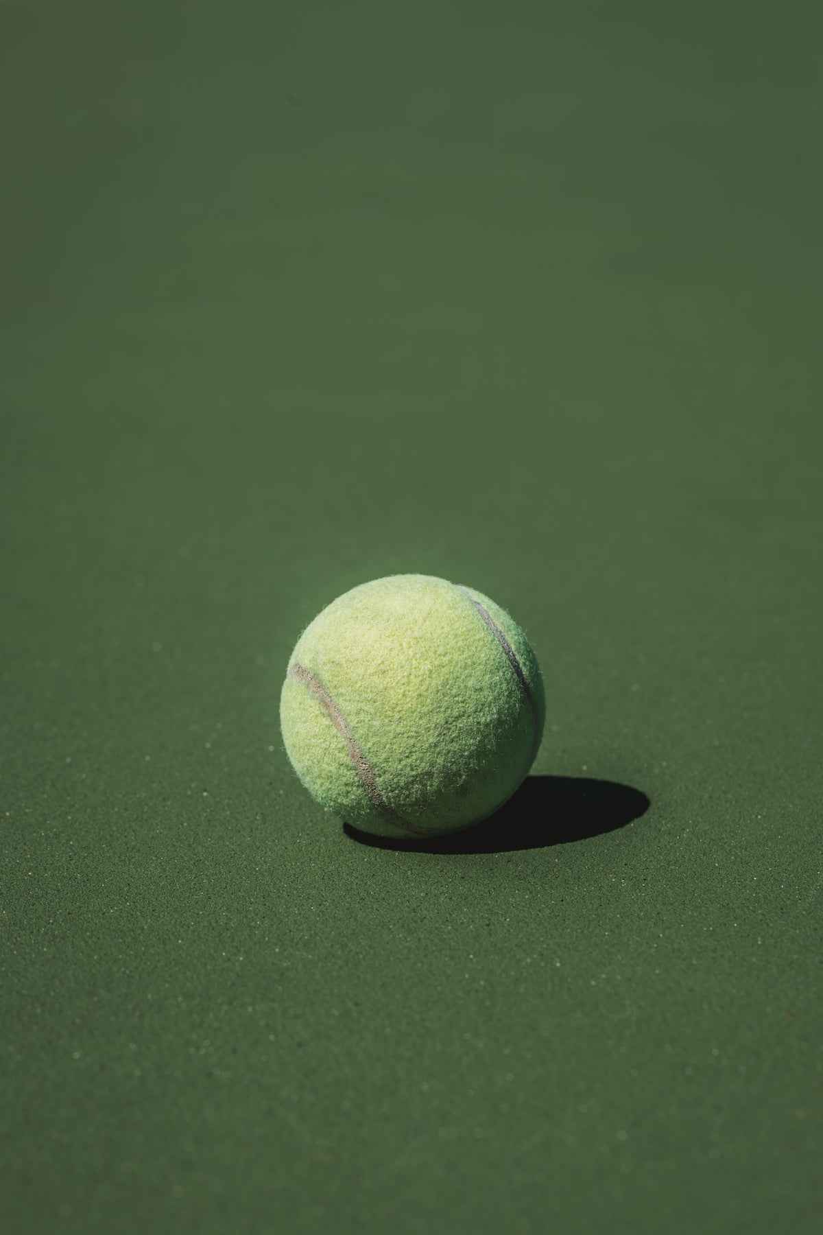 single tennis ball sits in the sun on the court