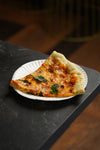 slice of pizza with fresh basil on a white paper plate