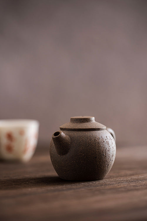 small brown teapot with a white and orange cup behind it