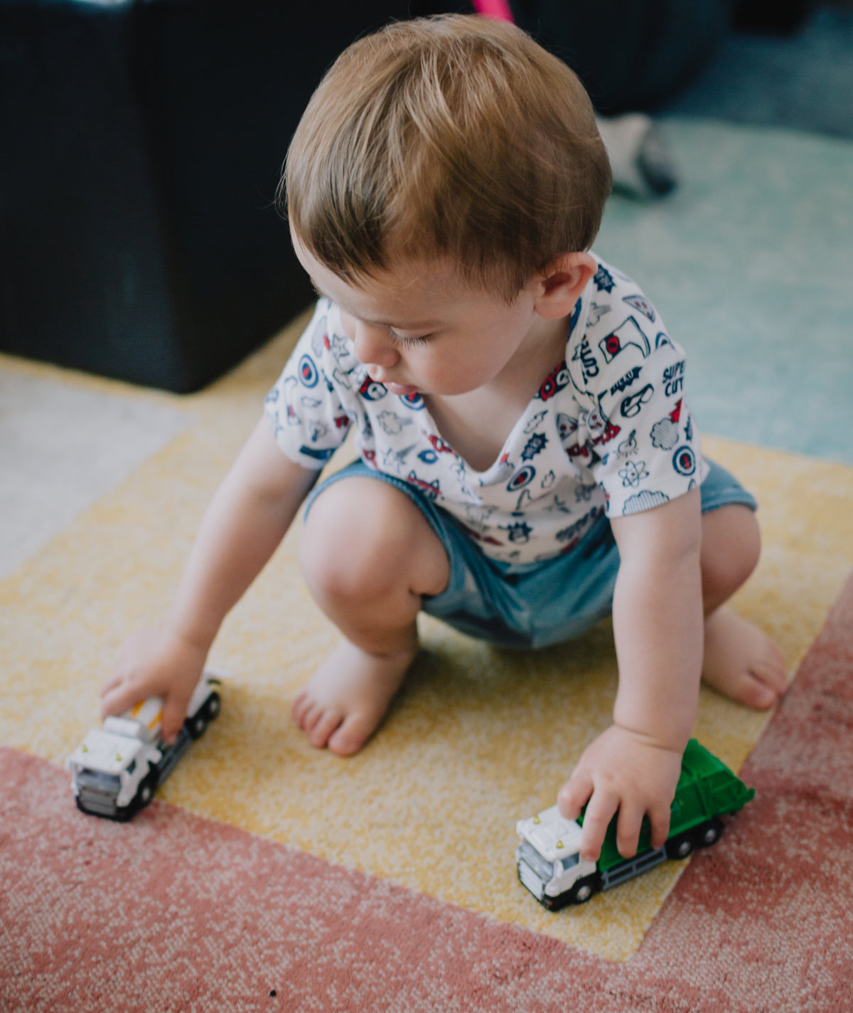 small child squats and plays with toy trucks