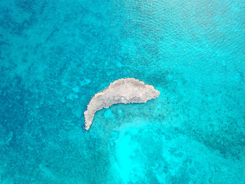 small rocky island in blue ocean shallows