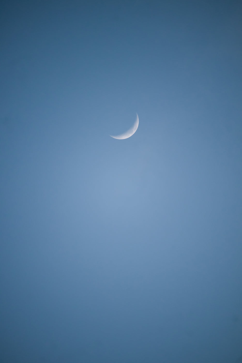 small sliver of the moon in a blue sky