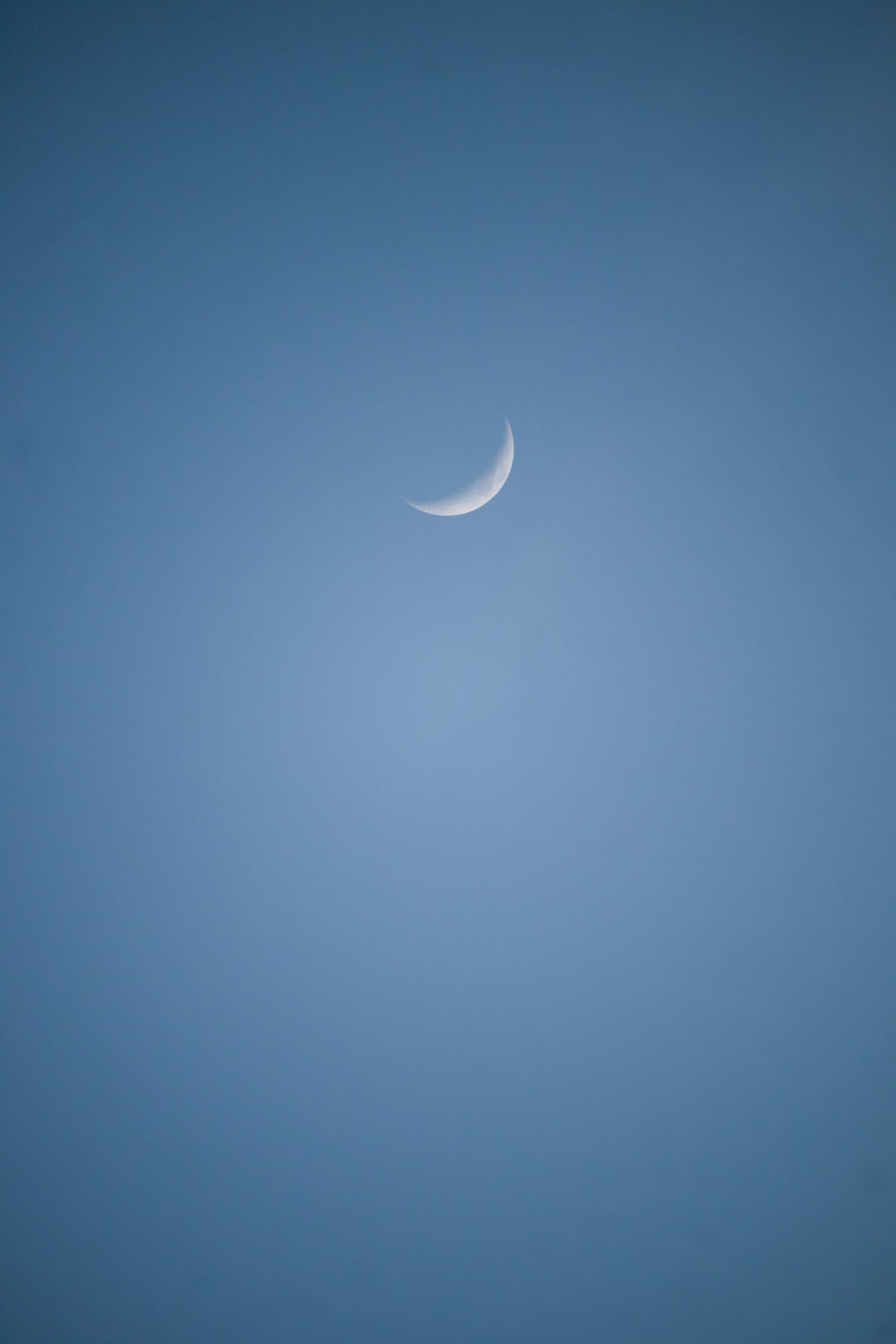 small sliver of the moon in a blue sky