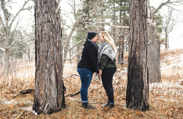 smiling couple stand nose to nose between two trees