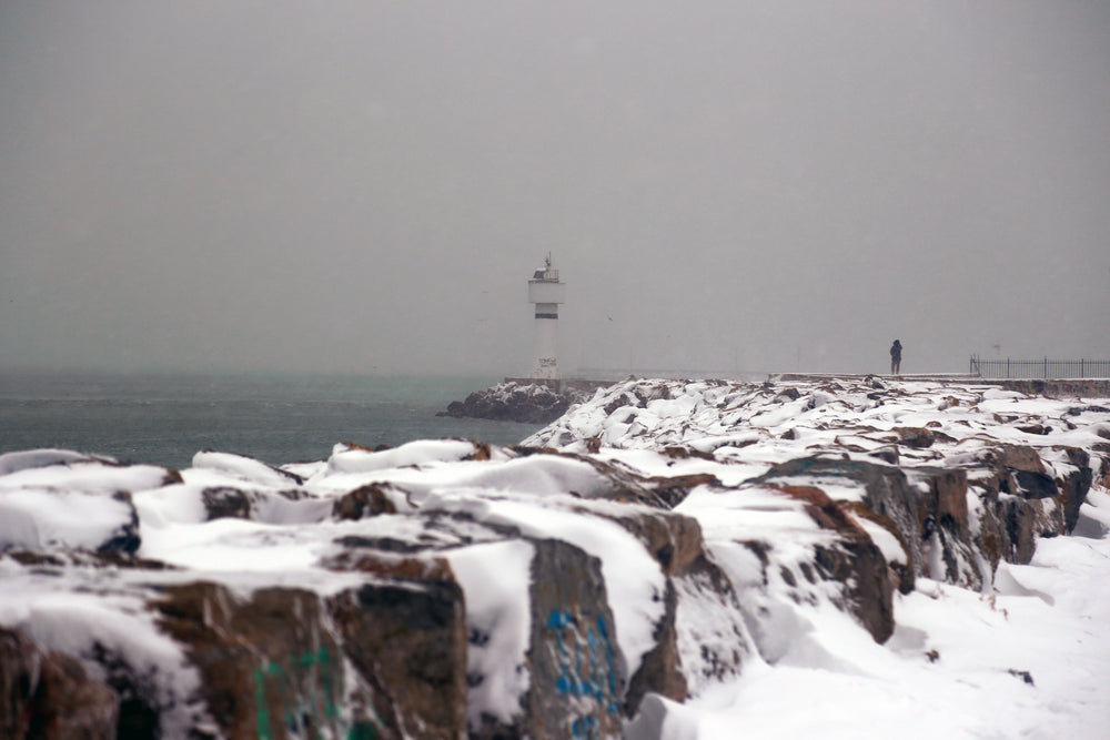 snow covered rocks and a lighthouse in frame