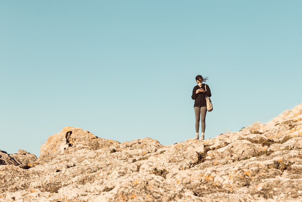 standing on rocky hill looking down at a phone