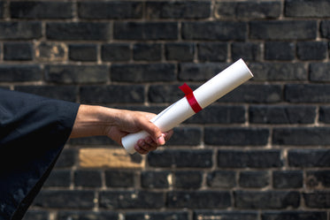 student holding out diploma by wall