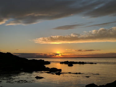 sun behind clouds at sunset by lake