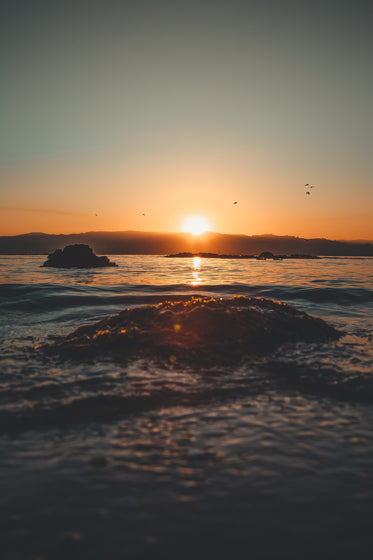 Sun Sets And Reflects On Water And Silhouettes Distant Hills