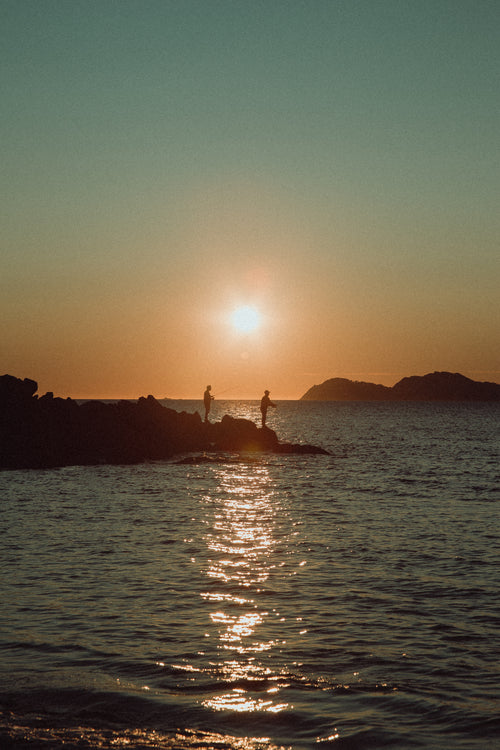 sun sets behind fishermen