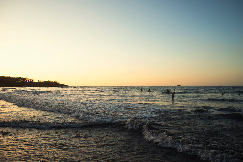 sun sets over surfers and beach goers