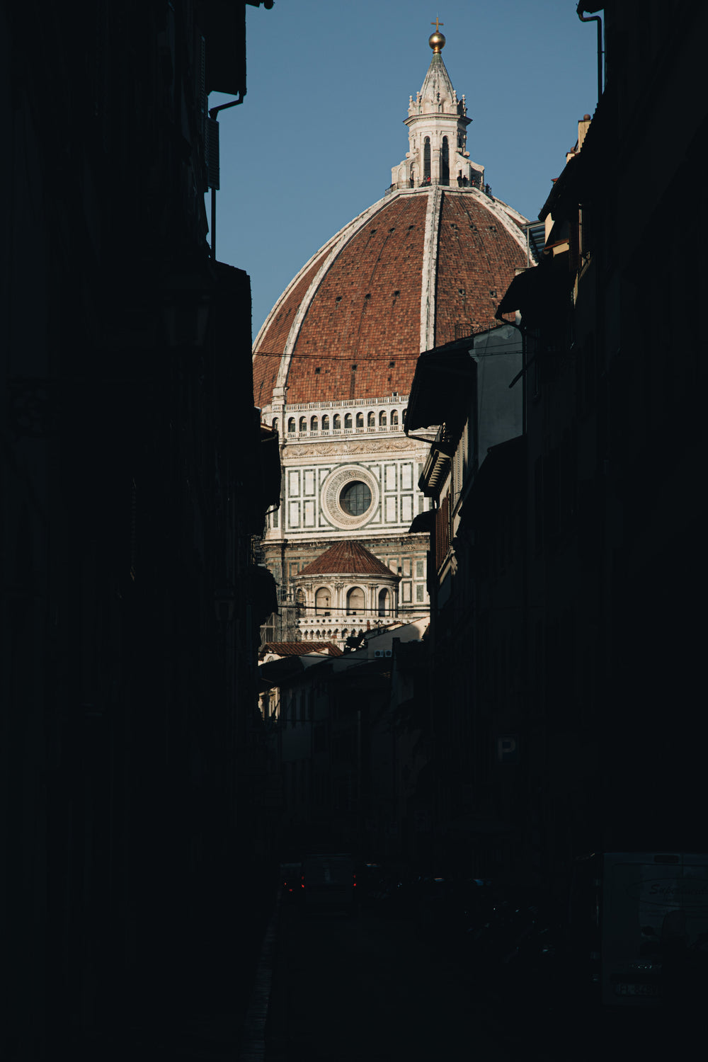 sun shines on church dome rising from dark streets