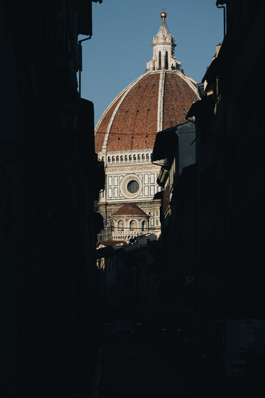 sun shines on church dome rising from dark streets