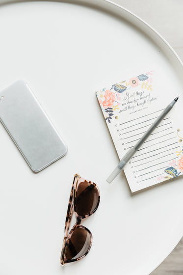 sunglasses, stationary, and a cellphone on a white tray