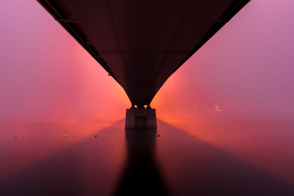 sunrises under a stone bridge creating a pink sky