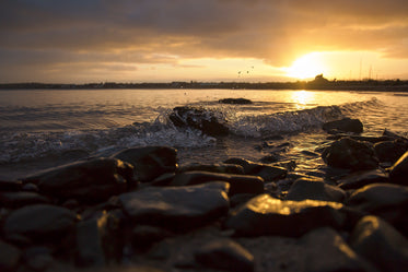 sunset against waves hitting rocks on the shore