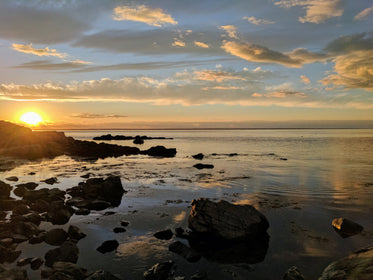 sunset over water by rocky shore