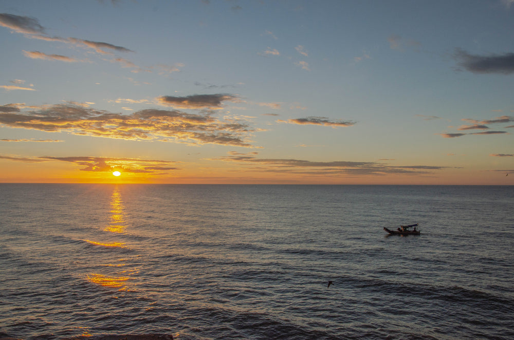 sunset silhouettes a boat riding on wavy water