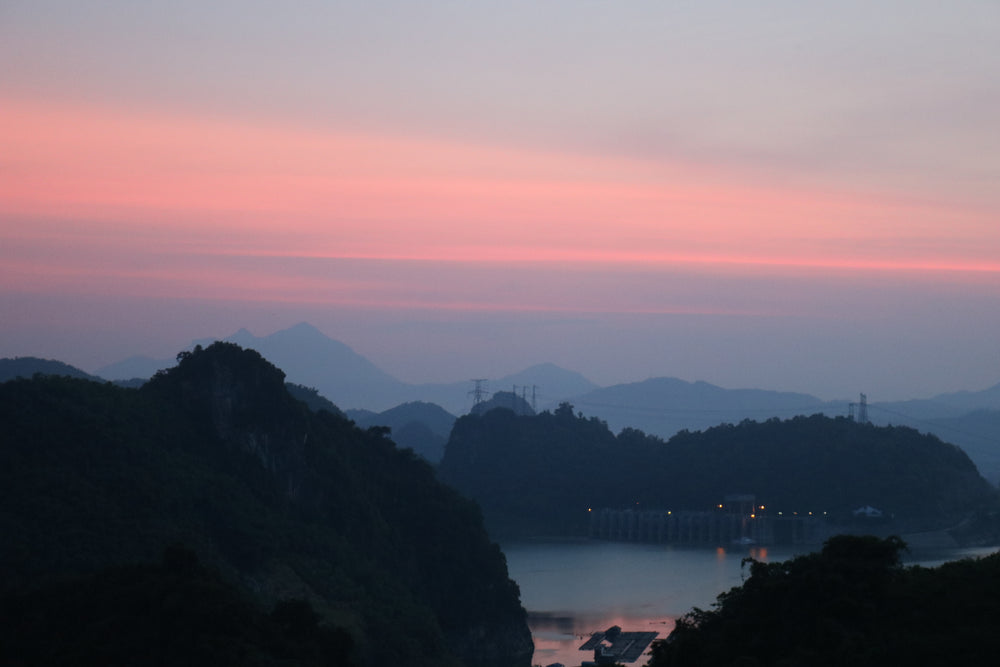 sunsets behind large tree covered hills and body of water