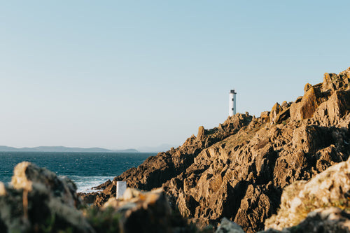高耸的灯塔矗立在陡峭的岩石海岸线上，映衬着蓝色的海水