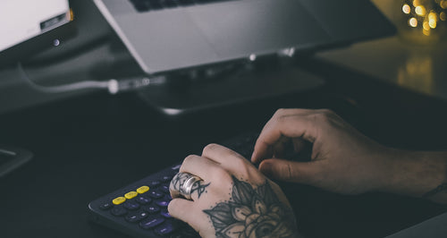 tattooed hands typing on office keyboard