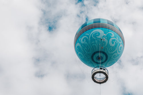 teal hot air balloon floats up into white puffy clouds