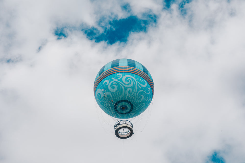 teal hot air balloon framed by puffy white clouds and blue sky