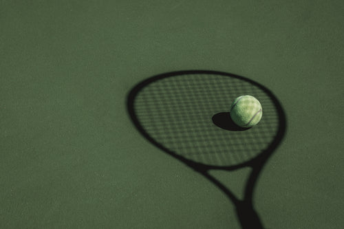 tennis ball sits in the shadow cast by a tennis racket
