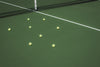 tennis balls sit on the green court bleached by the sun