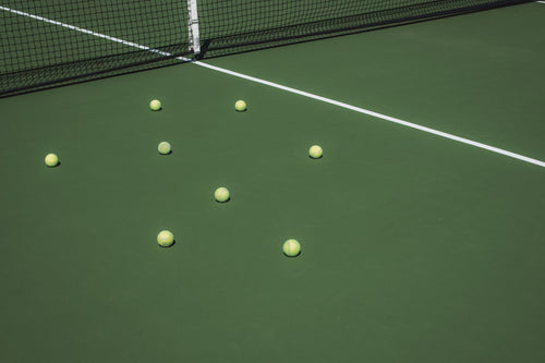 tennis balls sit on the green court bleached by the sun