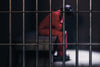 the faint shape of a prisoner behind black prison bars