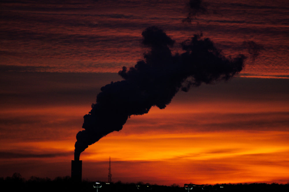 the silhouette of a smoke plume from a plant at sunset