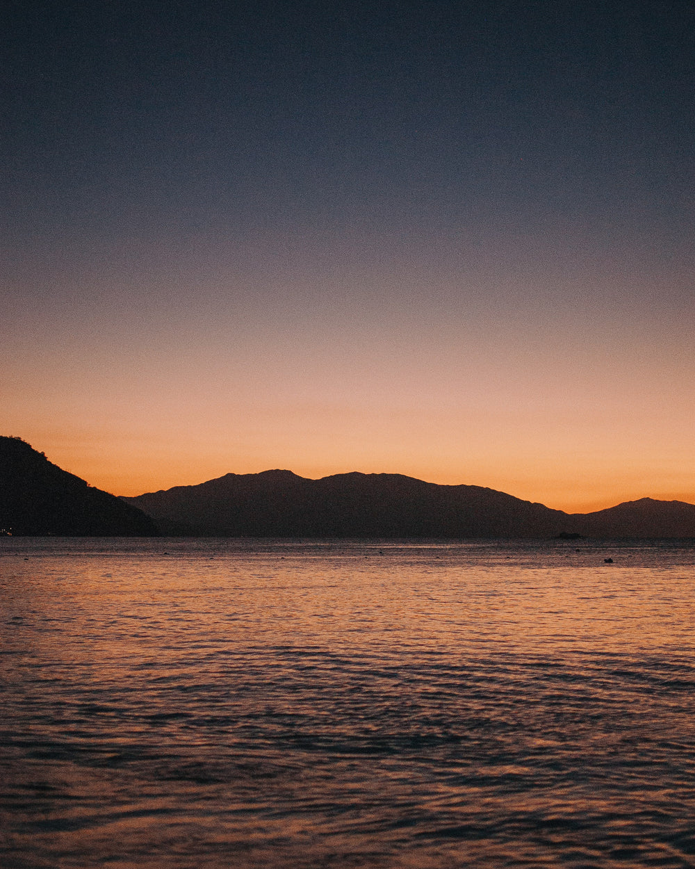 the sun sets behind the silhouette of seaside mountains