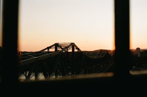 the sun sets on the steel trusses of a bridge