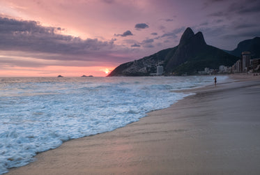 the sunrises over the water as a person walks the beach