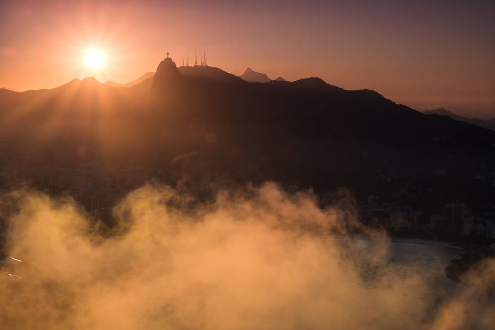 the sunsets behind a mountain with a small cross