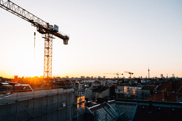 the sunsets over a city rooftops and tall cranes