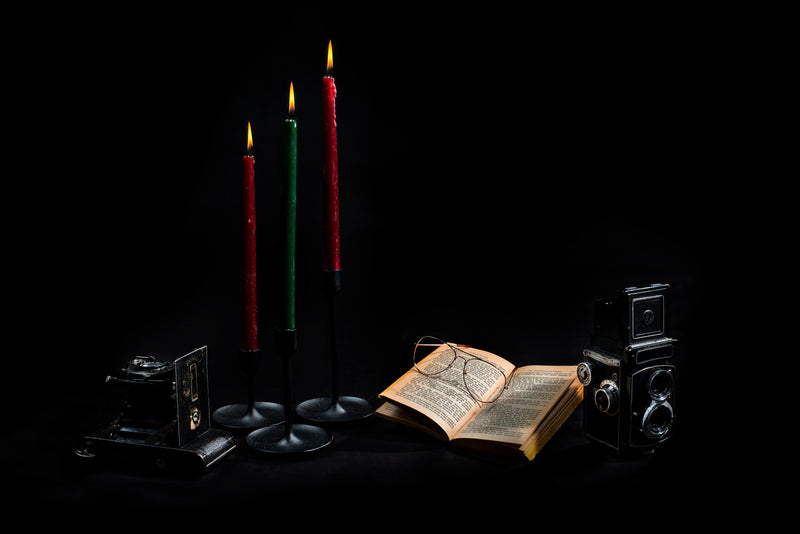 a candle, a book, and a candle on a black background - three candlesticks books and cameras