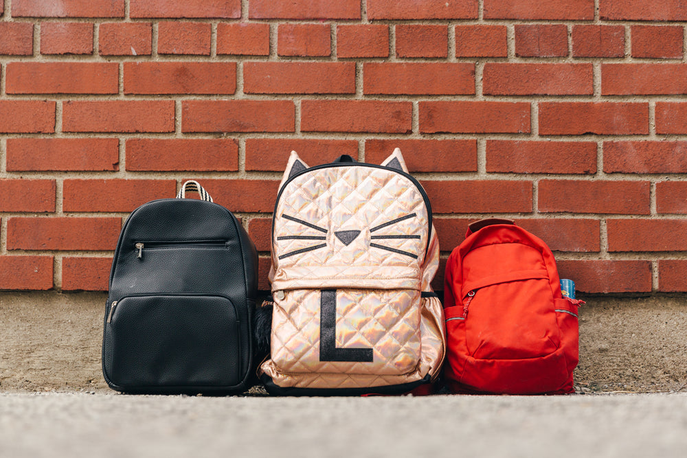 three children's backpacks along brick wall