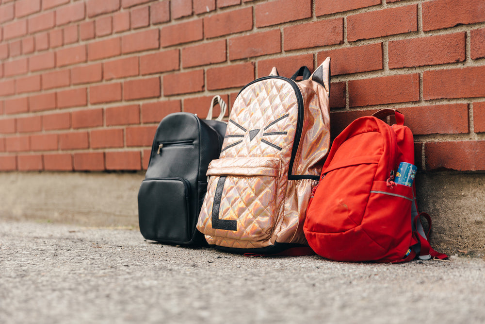 three children's backpacks and a brick wall