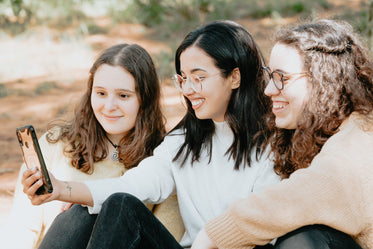 three friends sit outdoors while one looks at a cellphone