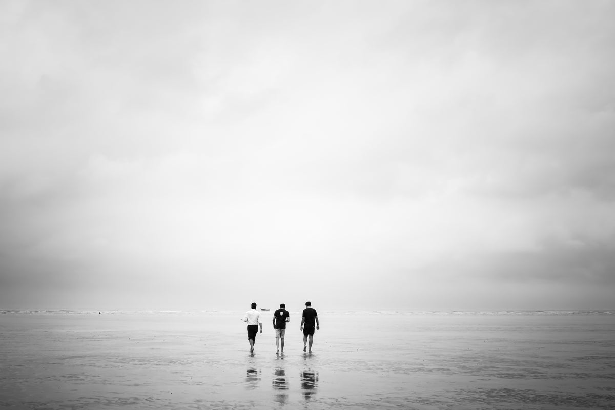 three men walk out over a low-tide beach