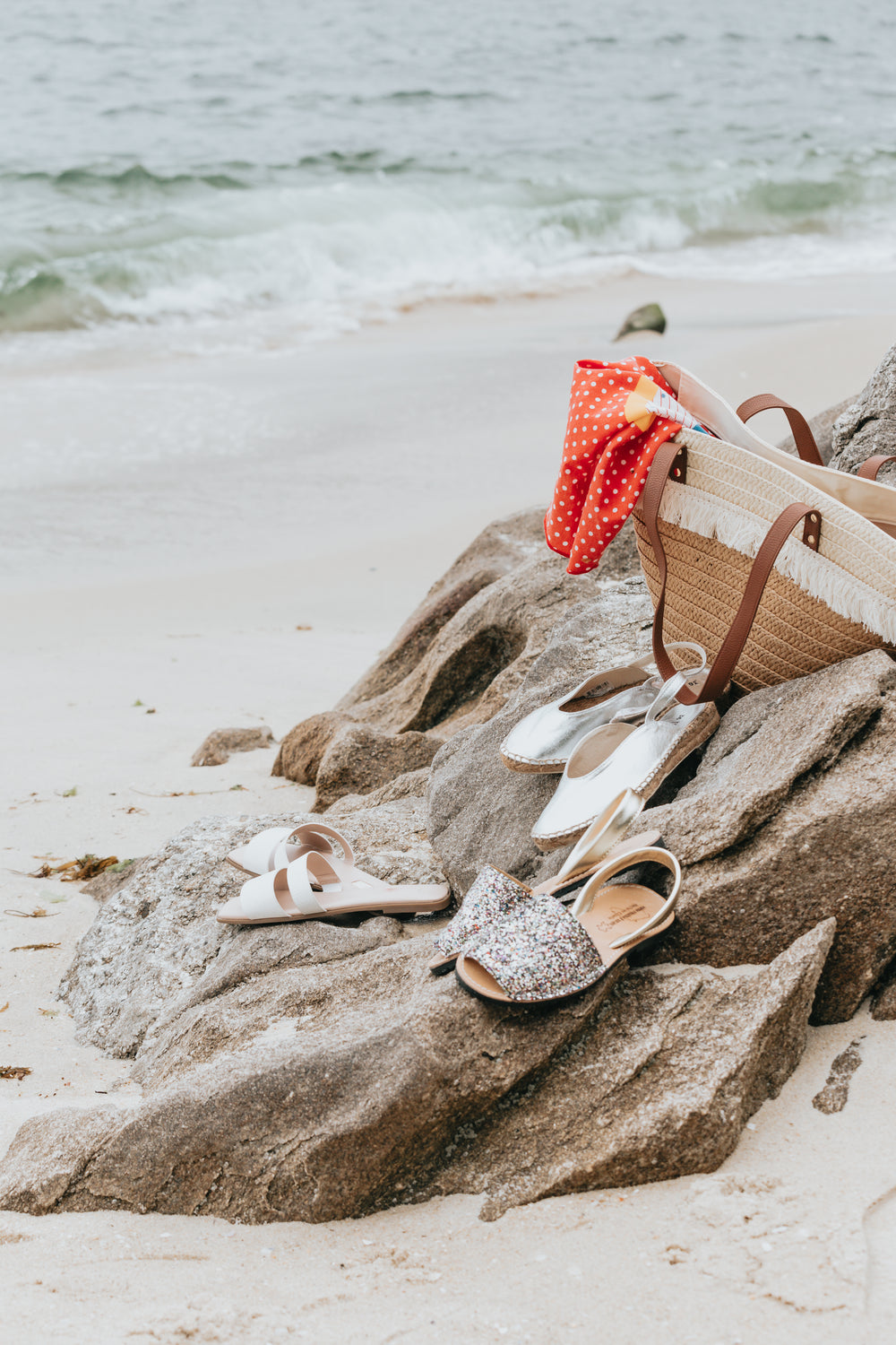 three pairs of summer shoes and a beach bag on the beach