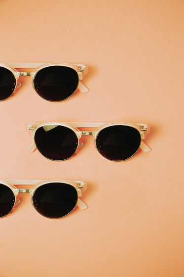 three pairs of sunglasses lay on a pink background