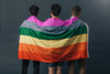 three people holding pride flag over their backs