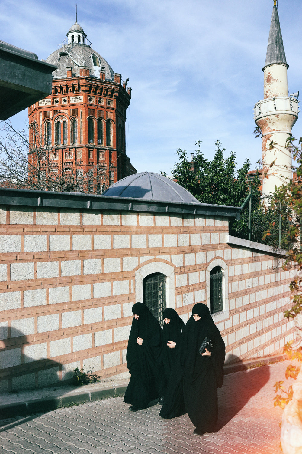 three people in all black walk up a city street together